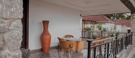 A balcony with a table and chairs, a large vase, and a railing.