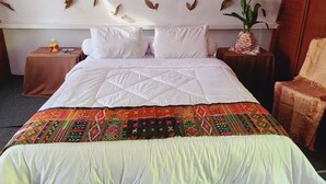 A bed with a white quilt, a patterned throw, and a wall decorated with dried leaves. - Pondok Wisata Noah (Likupang)
