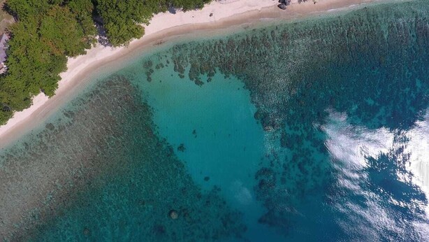 An aerial view of a beach with clear turquoise waters and a sandy shore. - Pondok Wisata Noah (Likupang)