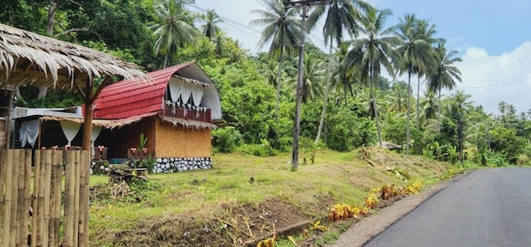 A rural house with a red roof, a thatched roof structure, and a small garden area. - Pondok Wisata Noah (Likupang)