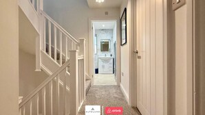 A hallway with a carpeted floor, white walls, and a door leading to a bathroom. - Available Now|Luxury|Contractors|Families|Groups (Easton)