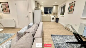 A modern apartment with a sofa, a dining table, a kitchen with a washing machine, and a glass railing. - Available Now|Luxury|Contractors|Families|Groups (Easton)