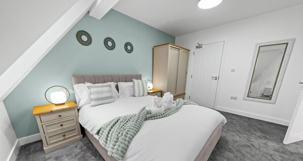 Une chambre à coucher comprenant un lit, des tables de chevet, une armoire, un miroir et une porte.