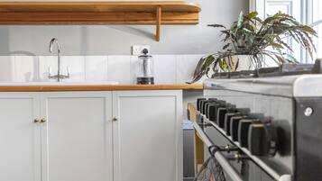 A kitchen with white cabinets, a wooden countertop, a coffee machine, and a plant.
