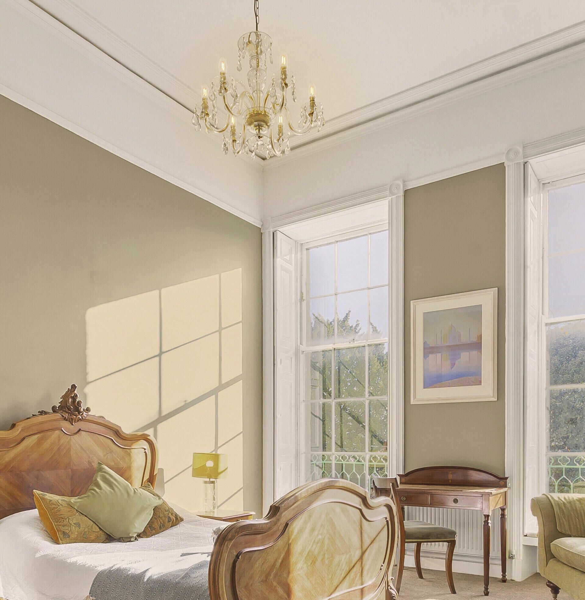 A bedroom with a large bed, a desk, and a chair. There is a window with a view of greenery outside.