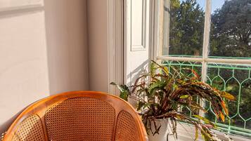 A wicker chair with a red cushion, a white table, and a potted plant with green and purple leaves.
