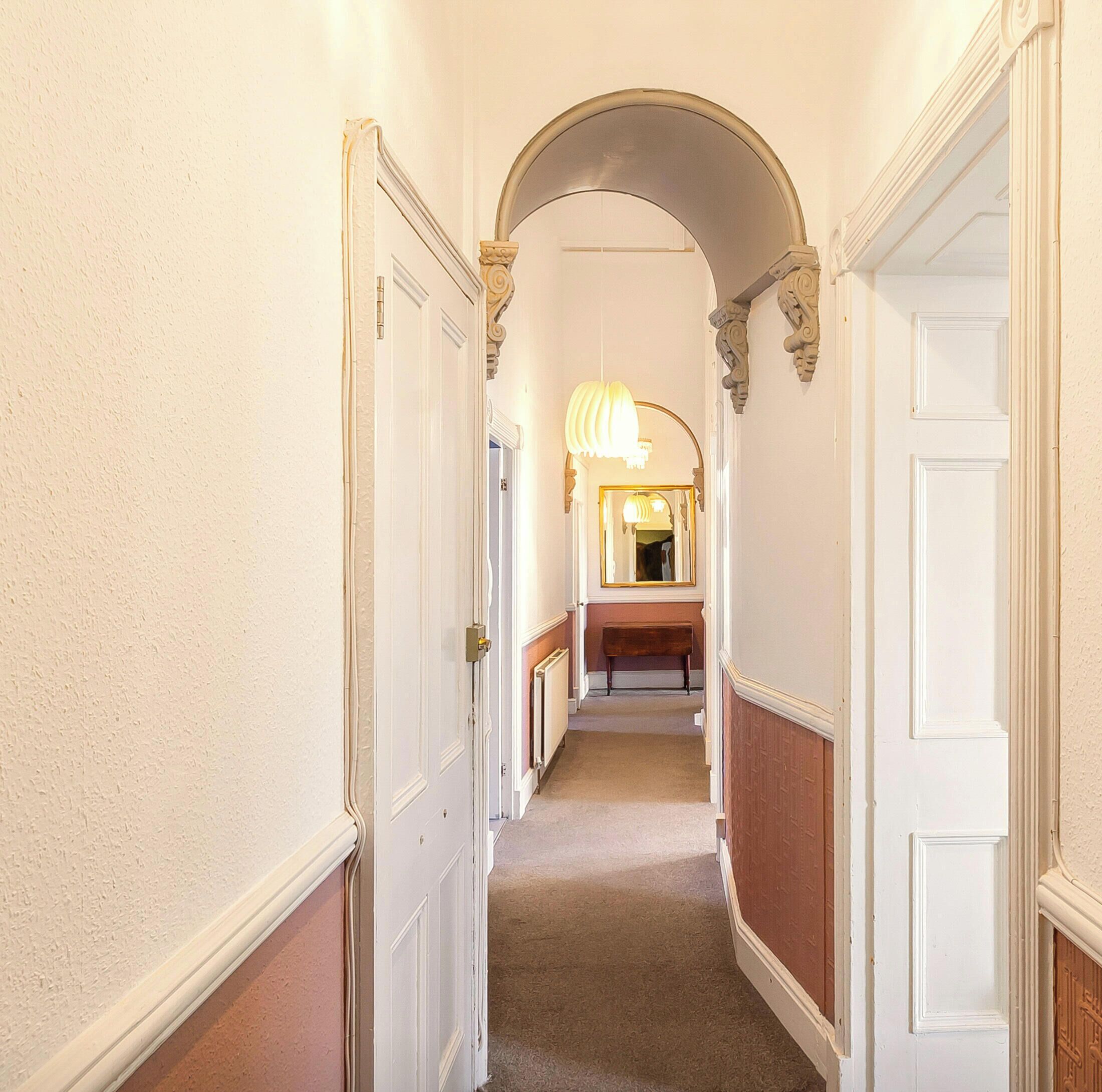 A hallway with white walls, a wooden bench, and a mirror reflecting a light fixture.