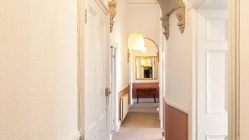 A hallway with white walls, a wooden bench, and a mirror reflecting a light fixture.