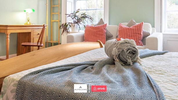 Una cama bien hecha con ropa de cama estampada, un cabecero de madera, un escritorio con lámpara, una silla y una ventana con vistas.