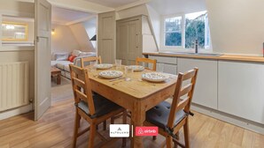 Un comedor con una mesa de madera dispuesta para cuatro, una ventana con vistas y una kitchenette al fondo.