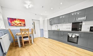 A modern kitchen with grey cabinets, a built-in oven, and a television mounted on the wall.