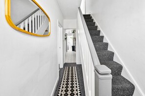 Un pasillo con una escalera, un espejo y piso estampado.