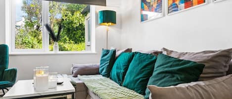 A modern living room with a sofa, a table, and a lamp. There are abstract paintings on the wall.
