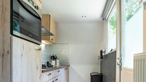 A narrow kitchen with wooden cabinets, a built-in oven, and a window. - Boshuisje met jacuzzi (Lanaken)