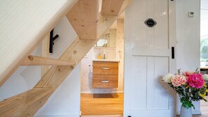 A wooden staircase leading to a room with a white door, a small bathroom, and a vase with flowers. - Boshuisje met jacuzzi (Lanaken)