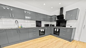 Een moderne keuken met grijze kastjes, een houten vloer en roestvrijstalen apparatuur.