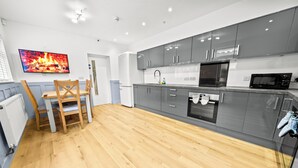 Een moderne keuken met grijze kastjes, een ingebouwde oven, een magnetron en een eethoek met een houten tafel en stoelen.