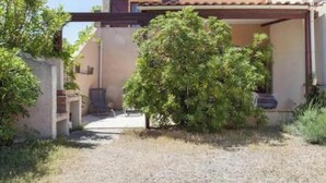 Un edificio con un espacio al aire libre techado, un camino de grava y un árbol pequeño.