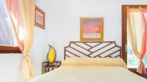 Un dormitorio con una cama, una mesita de noche, una lámpara, un cuadro en la pared y cortinas.