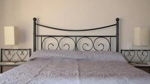 Una cama con cabecera de metal, colcha texturizada gris y dos mesitas de noche con lámparas.