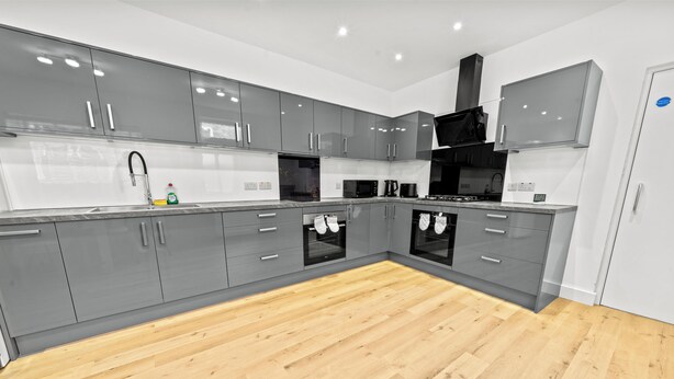 A modern kitchen with grey cabinets, a wooden floor, and stainless steel appliances. - Burnham-on-sea | Warm, Bright Ensuite Room | Ideal for Couple | Contractors Stay (Somerset)