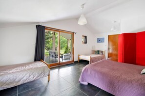 Una habitación con dos camas, una mesa de comedor, una silla y un ventanal corredizo que da a un espacio exterior.