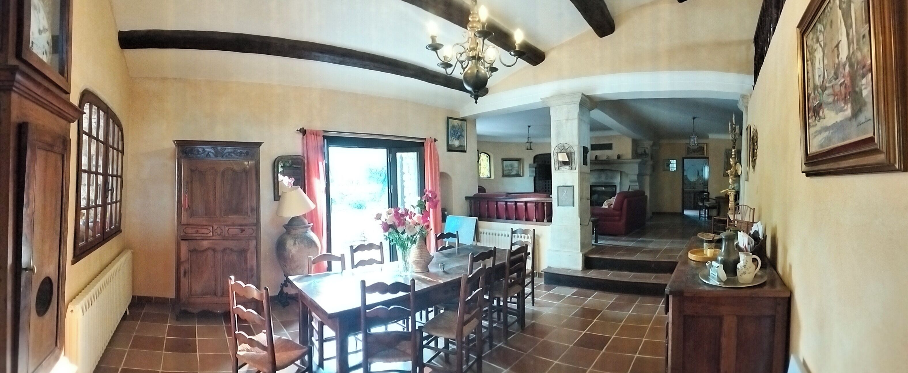 A dining area with a wooden table and chairs, a chandelier, and a view into another room.