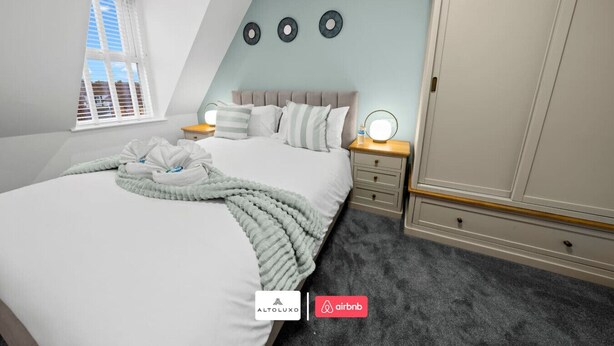 A bedroom with a bed, bedside tables, a wardrobe, and a window. - Burnham-on-sea | Luxury | Families | Large Groups (Somerset)