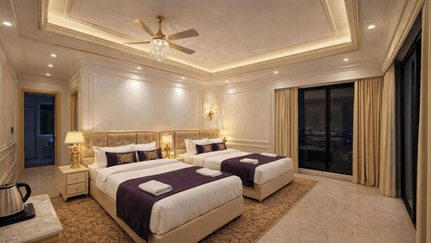 A hotel room with two beds, a ceiling fan, a chandelier, and a large window with curtains. - Narayana Grand Hotel (New Delhi)