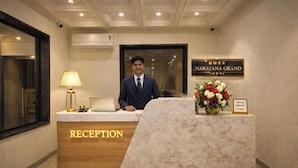 A hotel reception desk with a sign reading 'Hotel Narayana Grand,' a laptop, a lamp, and a floral arrangement. - Narayana Grand Hotel (New Delhi)