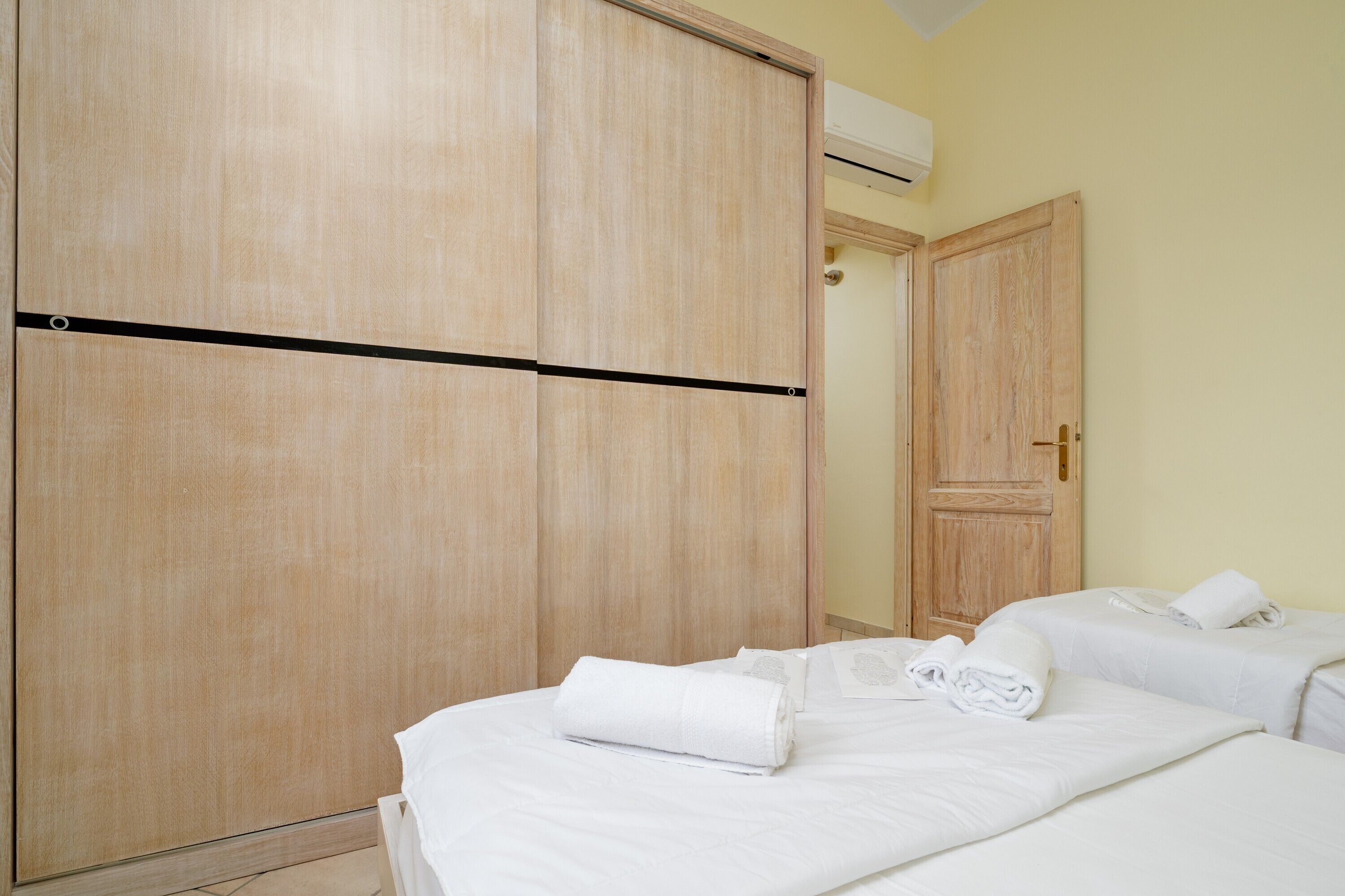 Habitació d'hotel amb un armari gran, dos llits amb roba blanca i una porta amb mànec de bronze.