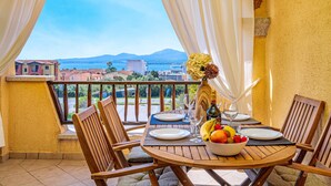 A balcony with a table set for two, a bowl of fruit, wine glasses, and a bottle.