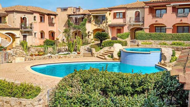 A resort with a swimming pool, multiple-story buildings, and a stone pathway.