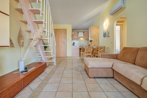 Una sala de estar con un sofá, una escalera, una cocina al fondo y un comedor.