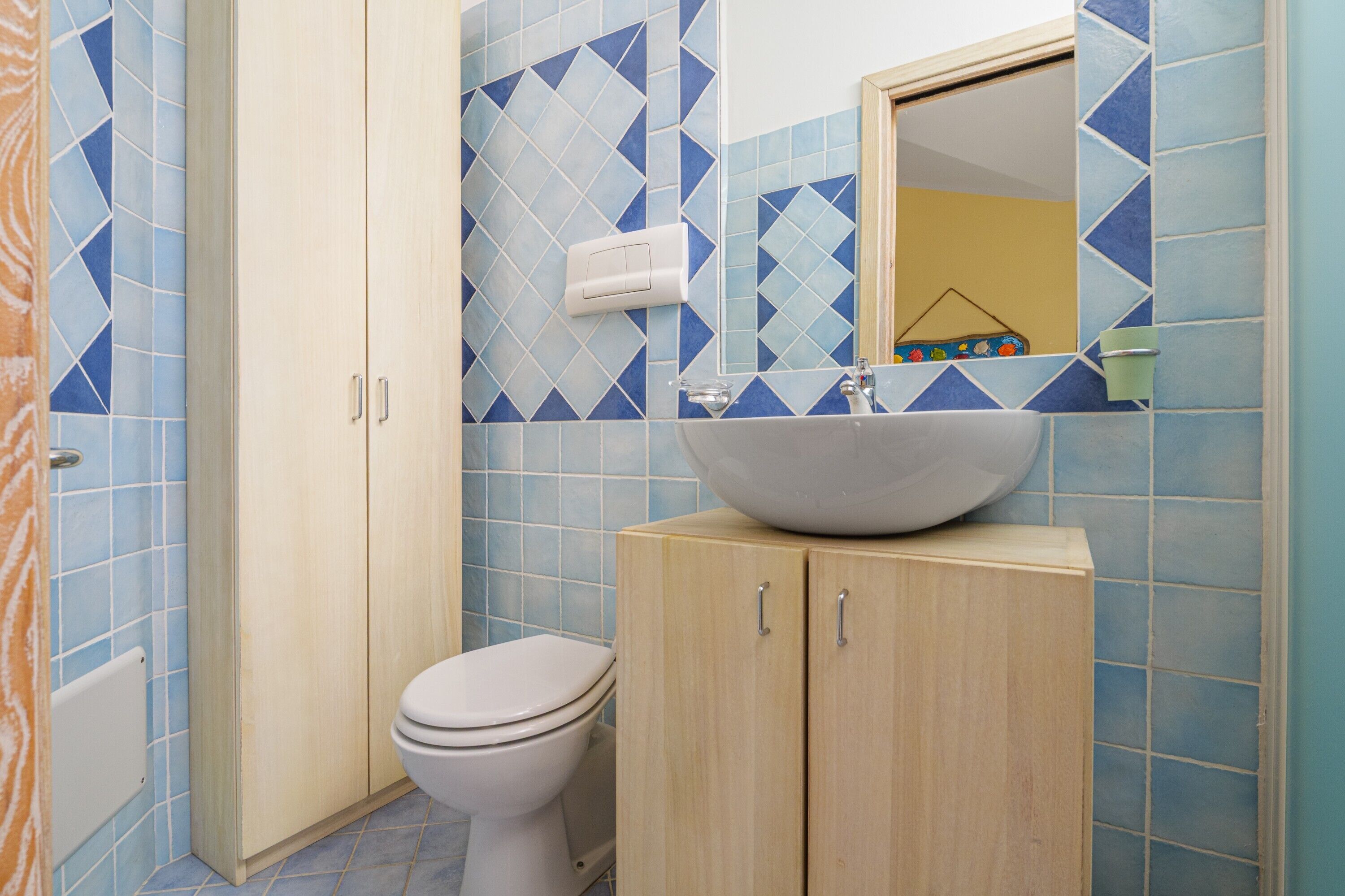 A bathroom with a toilet, a sink with a mirror above it, and cabinets.