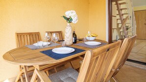 A wooden dining table with chairs, a vase with flowers, wine glasses, and a bottle.