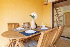 Una mesa de madera con sillas, un jarrón con flores, copas de vino y una botella.