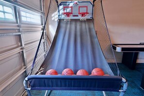 Ein Basketballkorb mit zwei Basketballsälen auf einer blauen Matte, eine Garagentür und ein Tisch mit Papieren.
