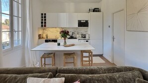 Une cuisine moderne avec des meubles blancs, un îlot central doté de tabourets et une table à manger.