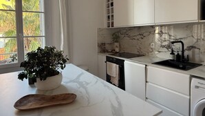 Une cuisine moderne avec des meubles blancs, un plan de travail en marbre, un évier noir et une fenêtre donnant sur un paysage verdoyant.