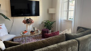 Un salon avec un canapé, une table basse, un téléviseur, une plante et une fenêtre avec des rideaux.