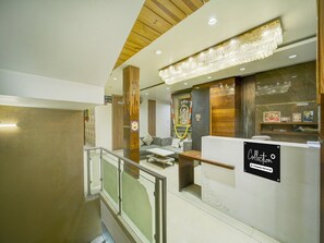 Zona de recepción de hotel con diseño moderno, que incluye un mostrador de recepción, una escalera y una araña.