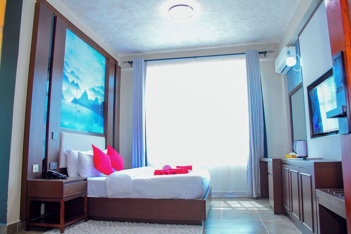 A hotel room with a bed, a nightstand, a TV, and a large window with curtains.
