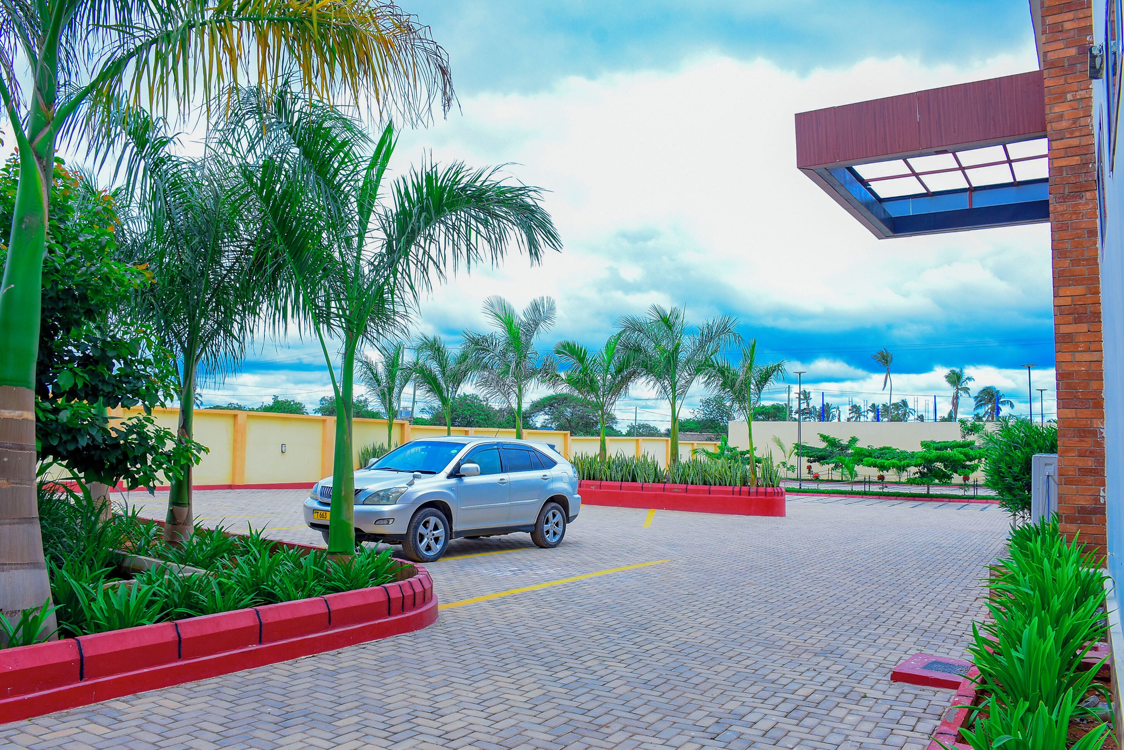 Un estacionamiento pavimentado con un automóvil, rodeado de vegetación y un edificio de fachada de ladrillo rojo.