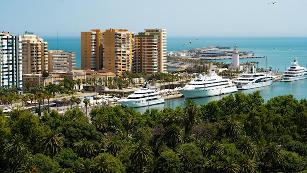 Eine Küstenstadtlandschaft mit Hochhäusern, einer Marina voller Yachten und einem Leuchtturm.