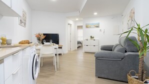 Eine moderne Küche mit Waschmaschine, Essbereich mit Tisch und Stühlen, ein graues Sofa und eine kleine Pflanze.