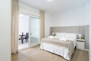 Ein Hotelzimmer mit Bett, Nachttisch, Lampe, einem kleinen Tisch mit Stühlen und einer Glastür zu einem Außenbereich.