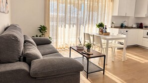 A modern living room with a grey sofa, a small coffee table, and a dining area with a white table and chairs. - Apartamento Don José BD (Malaga)