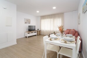 Ein modernes Wohnzimmer mit Esstisch für vier Personen, einem Flachbildfernseher und einer Couch.
