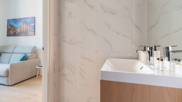 A modern bathroom with a marble wall, a white sink, and a mirror. - GuestHost - Comfortable 30m2 studio, perfect for 2, located on the second floor of a building with lift.The apartment is located in the Ca' Granda - Prato Centenaro area, located in Municipality 9 north of Milan, a well-connected residential area (M5 Ca' (Milan)